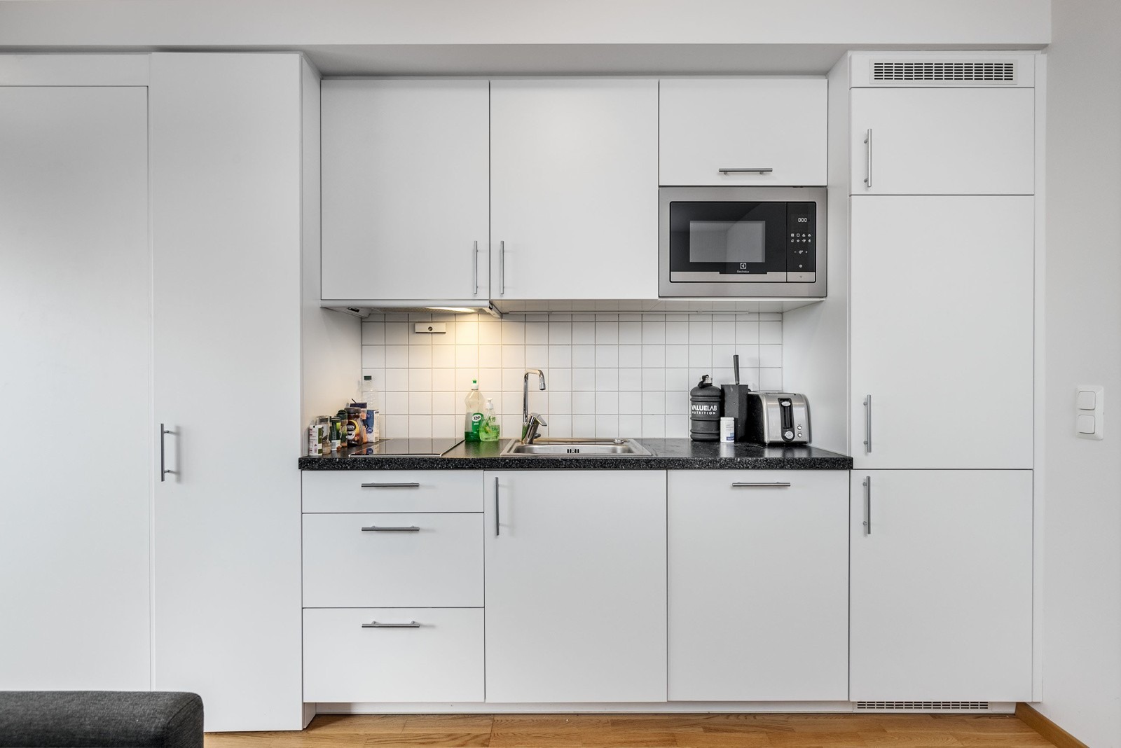 Stilrent og moderne kjøkken i åpen løsning. Innredning består av hvite slette skuffe- og skapfronter. Av utstyr finnes det integrerte hvitevarer som 2-soners induksjonsplatetopp, mikro, oppvaskmaskin, samt kombinert kjøl/frys.